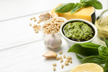 Fresh pesto sauce in bowl and ingredients on white wooden table. Space for text