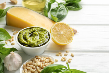 Fresh pesto sauce in bowl and ingredients on white wooden table. Space for text
