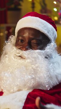 Santa Claus portrait thums up putting gifts under christmas tree in living room, making surprise. African american man in costume of Santa puts present box for children. Saint Nicholas working at