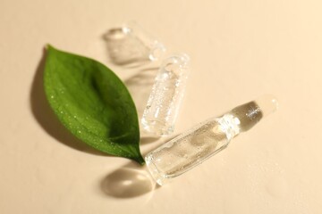 Glass ampoules with cosmetic product, leaf and water drops on beige background, closeup