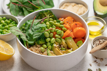White Bowl with with Healthy Quinoa Salad, Edamame Beans, Broccoli, Carrot, Lettuce Leaves and Avocado Surrounded by Ingredients  on Light Background, Clean Eating Concept