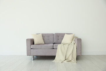 Comfortable gray sofa with blanket and cushions in room