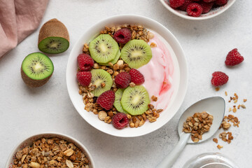 Top View of Raspberry Yogurt in White Bowl with Fresh Kiwi Topping and Ripe Raspberries on Bright Background, Healthy Dessert and Breakfast Concept