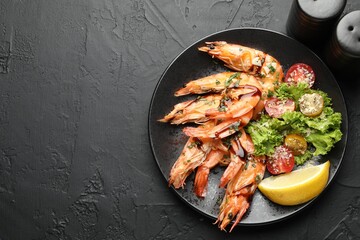 Delicious seafood dish. Tasty grilled shrimps served with salad and lemon on black table, flat lay. Space for text