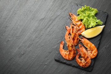 Delicious seafood dish. Tasty grilled shrimps with lemon and lettuce on black table, flat lay. Space for text