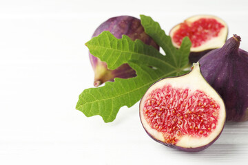 Fresh ripe figs and green leaf on white table, closeup. Space for text