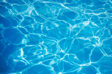 Clear blue swimming pool water surface with sunlight reflections and wave patterns creating abstract background