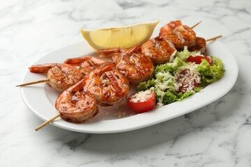 Skewers with tasty grilled shrimps, salad and lemon slice on white marble table, closeup. Delicious seafood dish