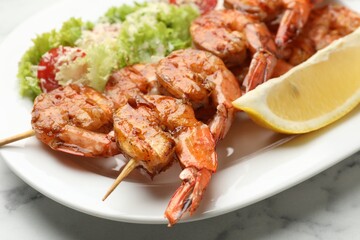 Skewers with tasty grilled shrimps, salad and lemon slice on white marble table, closeup. Delicious seafood dish