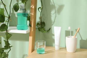 Glass of mouthwash, toothbrushes and toothpaste on shelf in bathroom