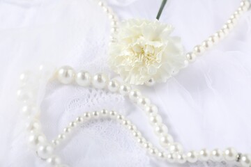 Beautiful pearl necklace and carnation flower on lace fabric, closeup