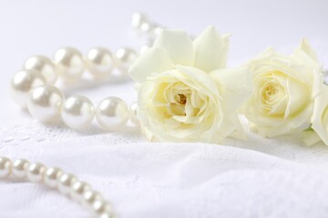 Beautiful pearl necklace and rose flowers on lace fabric, closeup