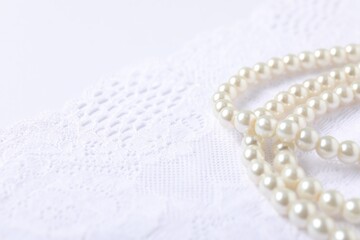Beautiful pearl necklace on lace fabric, closeup. Space for text