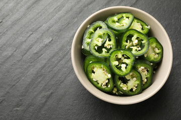 Pieces of green jalapeno peppers in bowl on grey table, top view. Space for text
