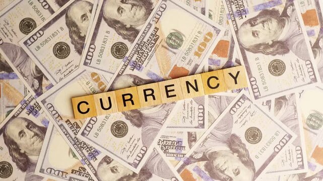 Wooden blocks with the letters "Currency" arranged on a slowly rotating stack of dollar bills. Looping 360-degree of wooden blocks with the words "Currenc" as a business financial concept. 4K footage.