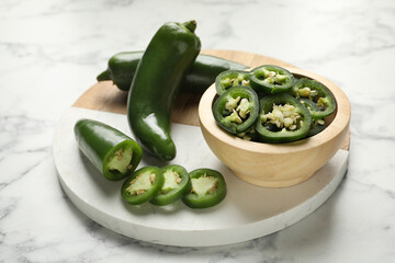 Whole and cut jalapeno peppers on white marble table, closeup
