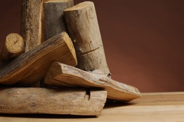 Pile of cut firewood on wooden table against brown background, closeup. Space for text