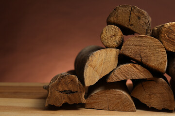 Pile of cut firewood on wooden table against brown background, closeup. Space for text