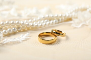 Beautiful golden rings and pearl necklace on lace fabric, closeup