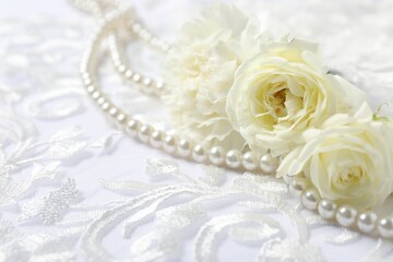 Beautiful pearl necklace and flowers on lace fabric, closeup. Space for text