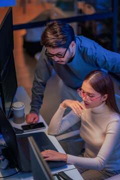 Asian programmers collaborating on software development at night, focused on writing code across multiple monitors in a tech office environment Programmers Collaborating on Software Development