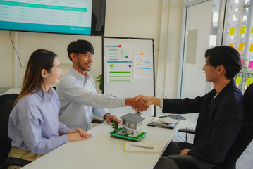 Closing the deal with paperwork and smiles. A couple shakes hands and thanks the real estate agent for the successful sale of their apartment, then concludes the deal and celebrates the purchase of th