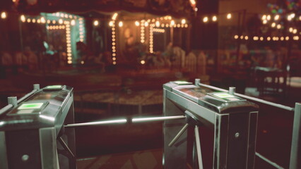 The entrance of an amusement park stands desolate at night, with turnstiles unoccupied and colorful lights casting a warm glow around. The atmosphere feels nostalgic and inviting.