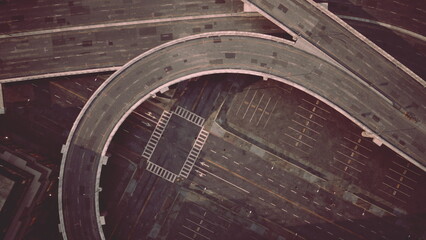 Aerial view of a busy urban interchange reveals a web of highways merging and diverging. The empty parking lots below contrast with the bustling roadways above, hinting at city life beyond the frame.