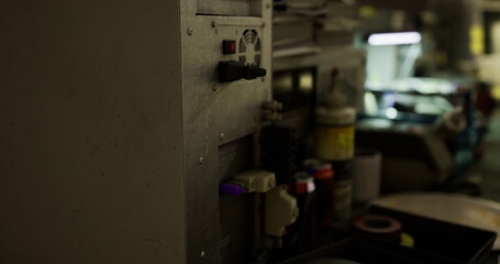 In a shadowy industrial setting, intricate machinery is highlighted, revealing various components. The focus lies on operational levers and gauges, conveying a sense of activity and purpose.