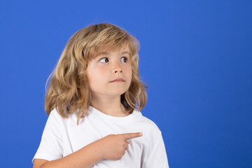 Cute child looking away, pointing finger on isolated studio background. Kid pointing to copyspace, showing promo offers, points away. Advertisement promo product concept.