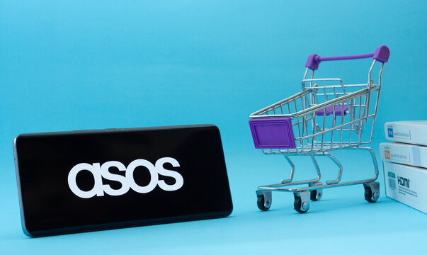 Dhaka, Bangladesh- 03 July 2025: Smartphone with ASOS logo next to a small shopping cart and boxes against a blue background.
