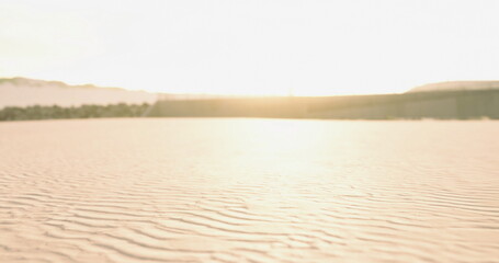 Bright sunlight reflects on gently rippling sand at the beach. Soft waves can be seen approaching the shore, creating a serene atmosphere at dawn. © icetray
