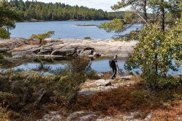 Back View of a Hiker Carrying a Knapsack and Walking Along the Rocky Shore of French River Ontario
