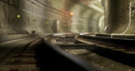 Obraz premium Curved rail tracks stretch into the darkness of a subterranean tunnel, with soft lighting illuminating the walls. The atmosphere feels quiet and isolated, hinting at the bustling activity above.