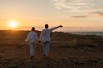 Fototapeta premium Couple Sunset Beach Walking - Silhouette of a couple walking hand in hand on the beach at sunset.