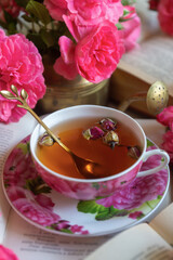 A cup of aromatic tea, a book and a rose on the table.