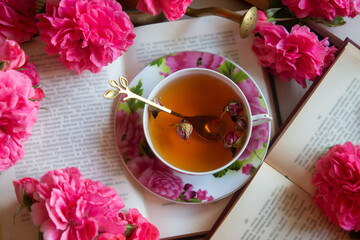 A cup of aromatic tea, a book and a rose on the table.