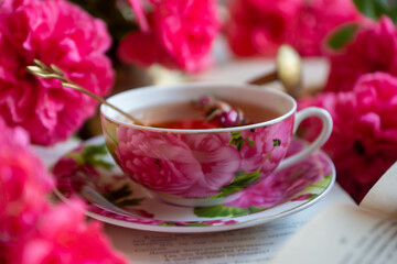 A cup of aromatic tea, a book and a rose on the table.