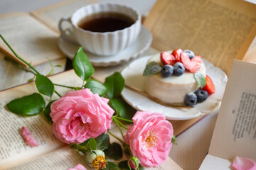 A cup of aromatic tea, a book and a rose on the table.