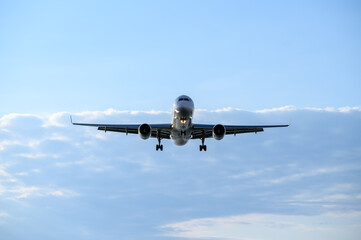 Large passenger jet flying in cloudy blue sky. Unmarked commercial aircraft taking off or landing. Air travel concept, air transport, passenger transportation, turbulence of liner in cloudy weather