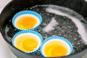 Three poached eggs cooking in blue silicone molds in boiling water on a stove