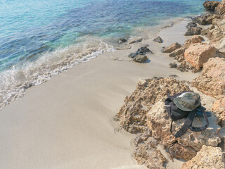 A pile of clothes with a cap above left at the rocky shore of a beach before going to swim to the beautiful blue Mediterranean sea at Nissi beach in Ayia Napa, Cyprus.