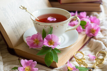 A cup of aromatic tea, a book and a rose on the table.