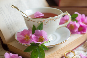 A cup of aromatic tea, a book and a rose on the table.