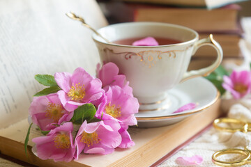 A cup of aromatic tea, a book and a rose on the table.