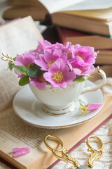 A cup of aromatic tea, a book and a rose on the table.