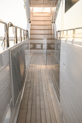 Narrow side deck of a modern luxury yacht featuring teak wood flooring, stainless steel railings, and an elegant stairway leading to the upper deck. 