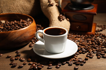 Aromatic coffee in cup, beans and grinder on wooden table, closeup