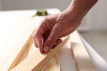 Man with metal nail and wooden planks at table indoors, closeup