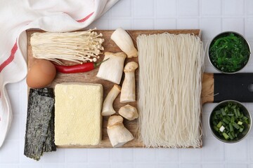 Enoki, king oyster (eryngii) mushrooms and other ingredients for ramen on white tiled table, flat lay